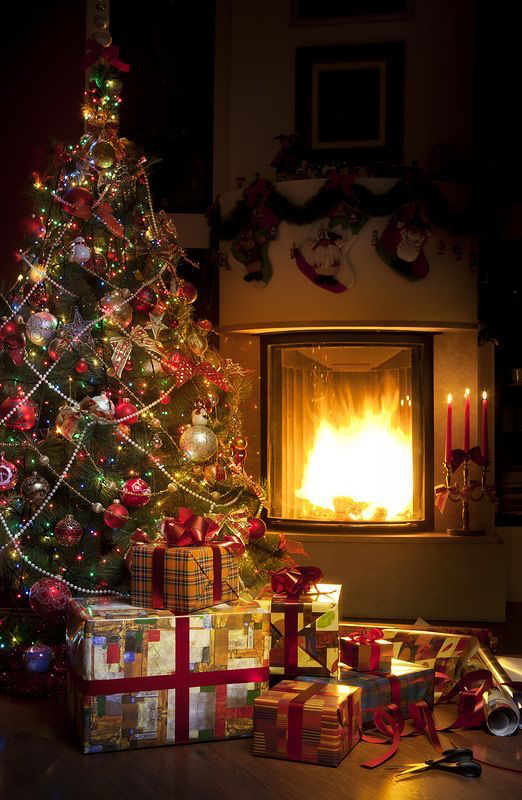 A Christmas tree next to a roaring fire and gifts on the table.