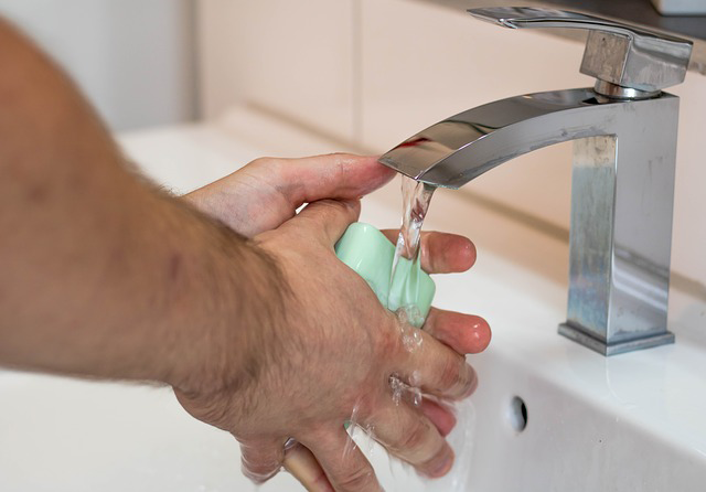 Close-up of a man's hands washing up with green soap under a sink faucet
