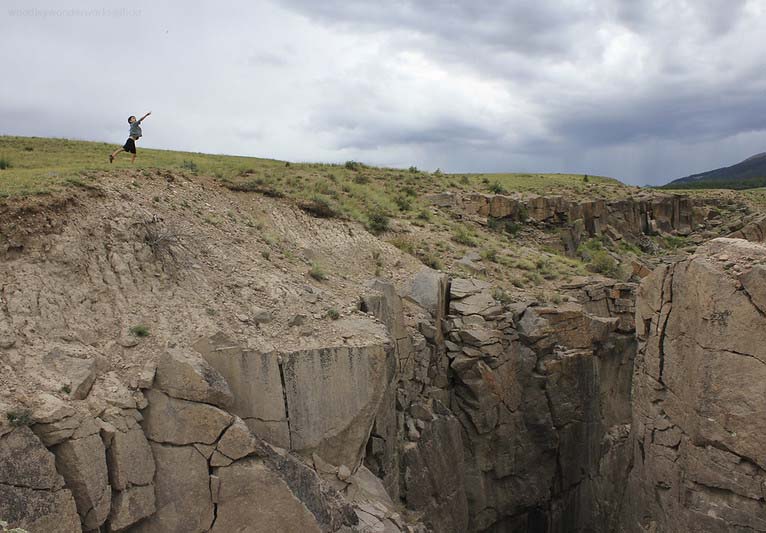 Under a stormy sky, a young boy stands above an abyss throwing rocks.