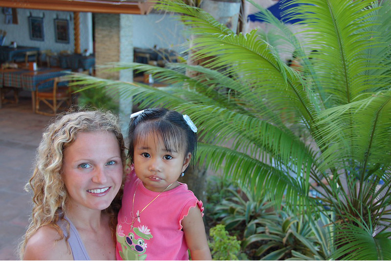 A curly-haired blonde woman holding a cute Filipino girl.