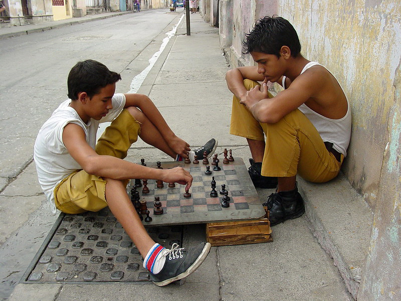 Spanning the sidewalk, two boys in yellow pants and white shirts play chess.