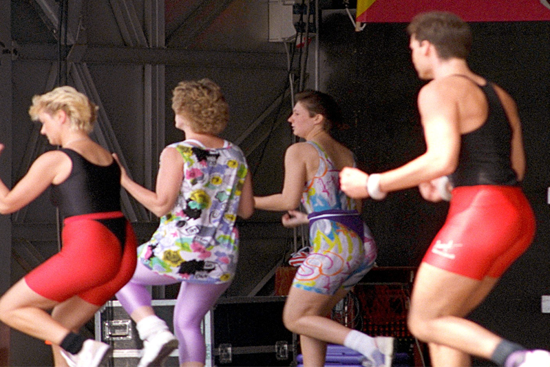 A public demonstration of aerobic exercises by three women and a man with their backs to us