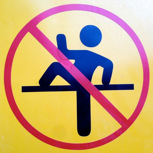 A yellow background has a red circle with a slash through it with the silhouette of a person with one leg and one arm on a horizontal bar.