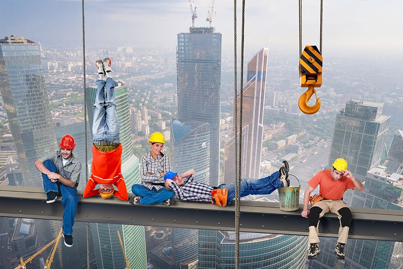Construction workers in various poses while high on a steel girder above the city