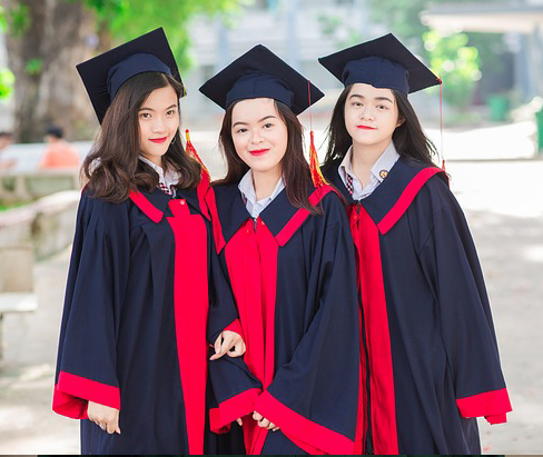 Three women graduates in gowns bordered in red and mortarboards