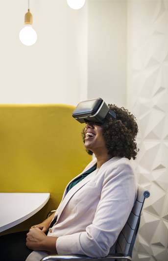 Wearing a white suit jacket, a woman is laughing while wearing a VR Headset.