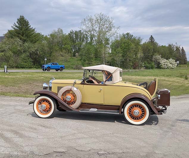 A butter yellow two-seater convertible with a rumble seat and orange spokes on the tires.