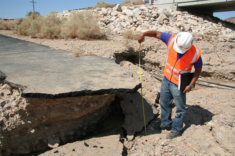 Engineer in orange safety vest measures the depth of the crevasse when a road broke.