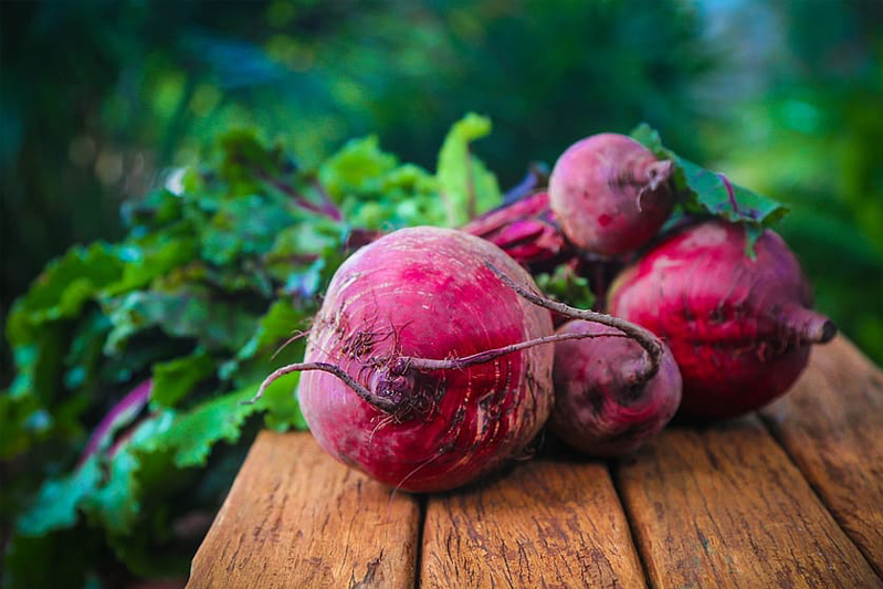 Foreshortened image of four beets with their leaves on a rough wood plank table.