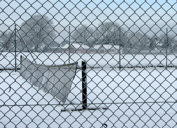 A tennis net blowing in the breeze with snow lying on the ground