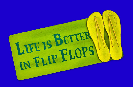 Against a royal blue background, a rounded rectangle in a distressed lime green with blue text that says Life is Better in Flip Flops with a pair of yellow flip-flops to the right of the sign