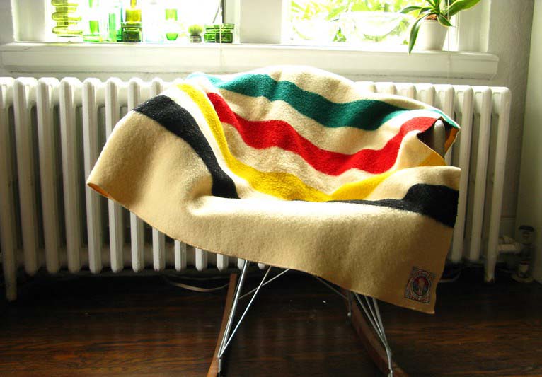 A Pendleton blanket with green, red, yellow, and black stripes against a cream background.