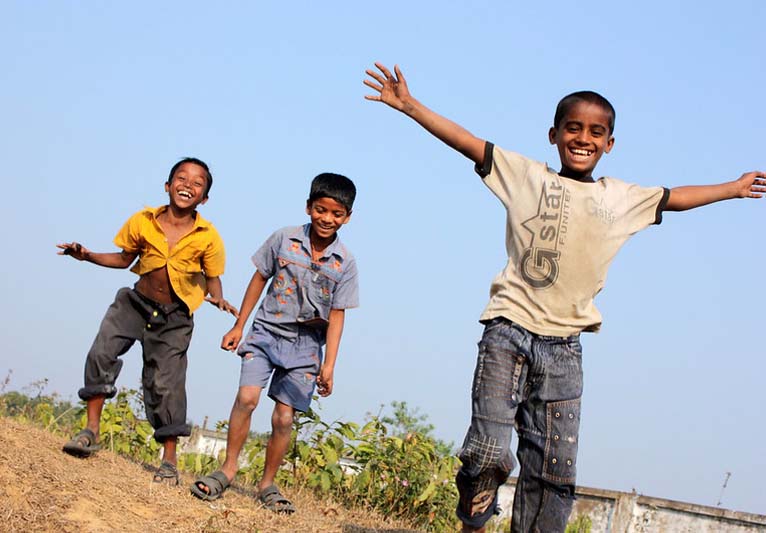 Three young boys standing on a hill under a blue sky wearing expressions of joy.