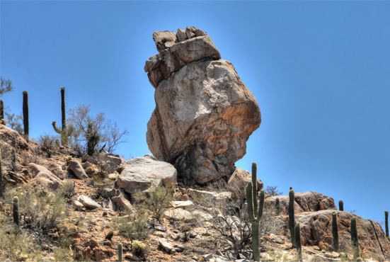 A pile of increasingly larger boulders perched on a cactus-studded slope.