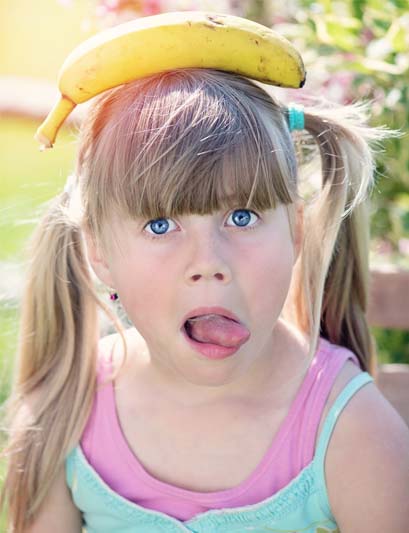 Young blonde girl with a banana on her head and sticking out a twisted tongue