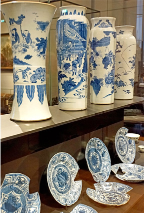 The wider bottom shelf displays seven broken blue-and-white plates while the narrower shelf above displays four tall blue-and-white vases.