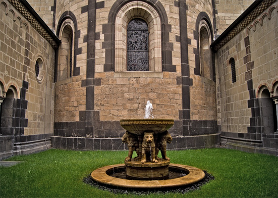 A fountain in the middle of a small churchyard enclosed by stone walls and grass