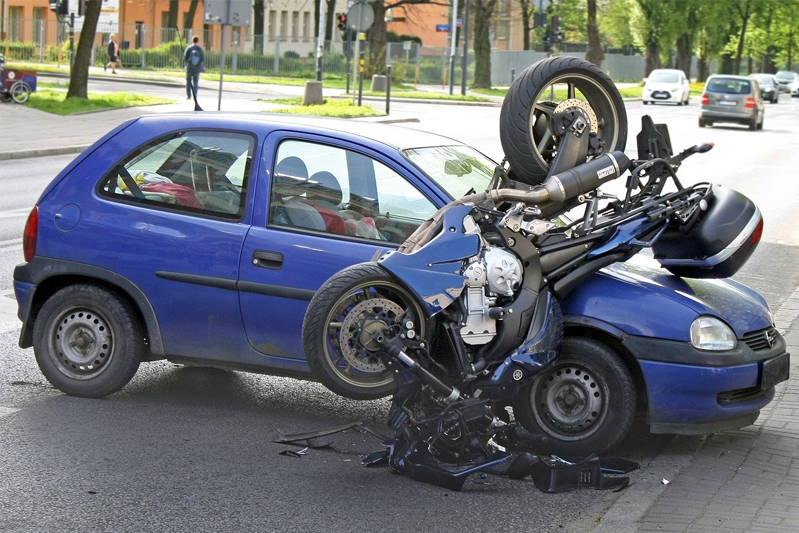 A blue motorcycle crashed into a small blue car.