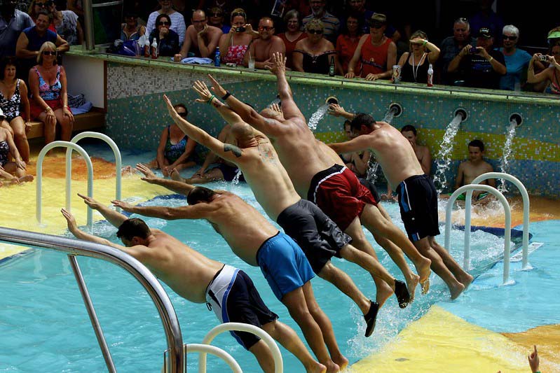 Surrounded by people, five men leap from the edge of the pool.