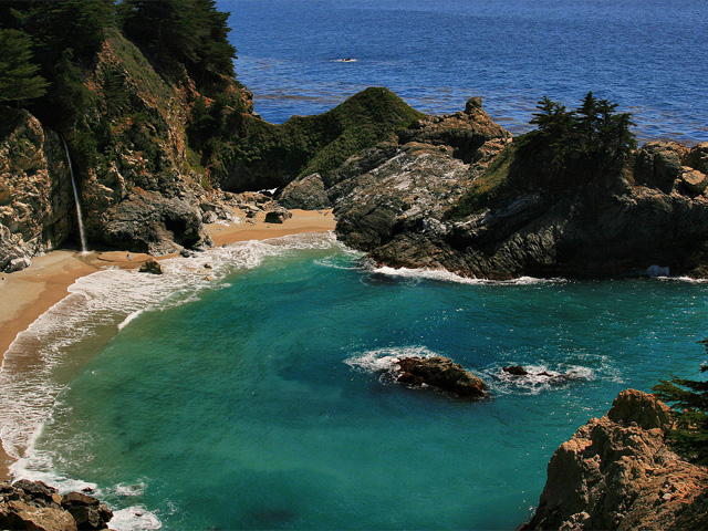 An aerial view of a small, enclosed cove surrounded by rocks with a narrow opening to the sea.