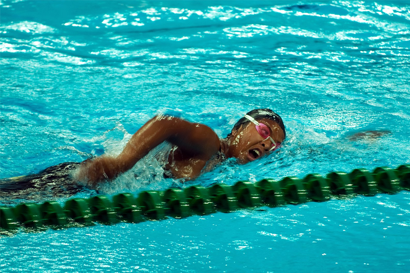 A swimmer in a blue pool is doing the crawl