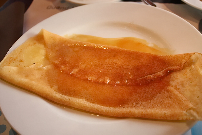 A white plate with a thin pancake folded over orange butter and covered in Grand Marnier
