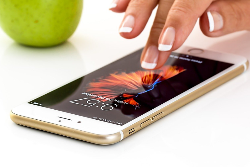 An iPhone lying on a white tabletop as a woman's fingers tap its screen.