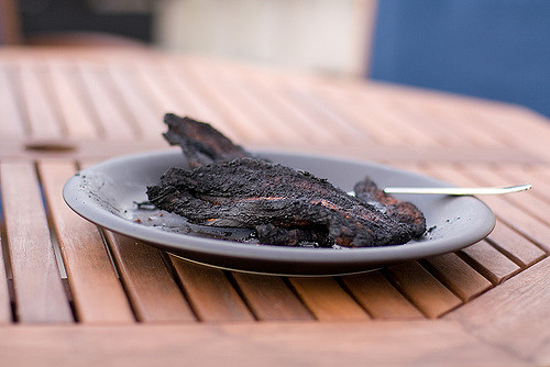 A gray plate of burned meat on a wooden slatted hexagonal table