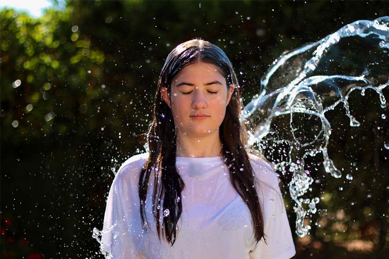 Woman with long black hair and wearing a white T-shirt has water thrown over her.