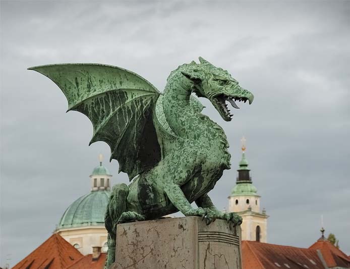 Part of the city skyline, a verdigris'd bronze dragon crouches atop a plinth and roars.