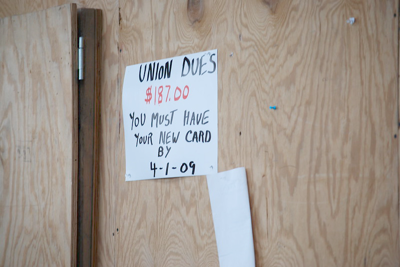 Handwritten sign about paying dues posted on a sheet of plywood