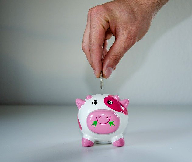 A hand is dropping a coin into a happy piggy bank
