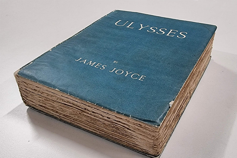 Positioned on an angle is a blue cloth-bound edition of Ulysses with the author's name, both in silver.