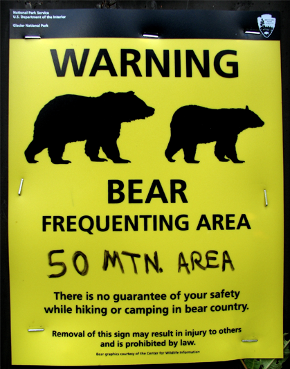 A rectangular yellow sign with black text warning about bears in the area