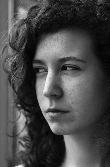 A black-and-white three-quarter profile of a woman with long curly hair and a mean look on her face