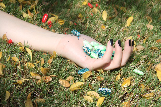 Woman's arm with a hand full of drugs lying on green grass
