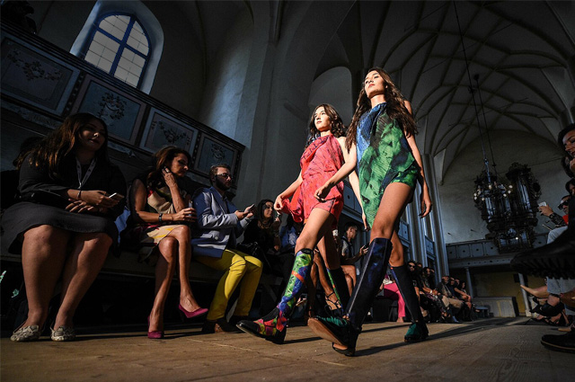 Two models in bright fashions walk down the aisel of a church