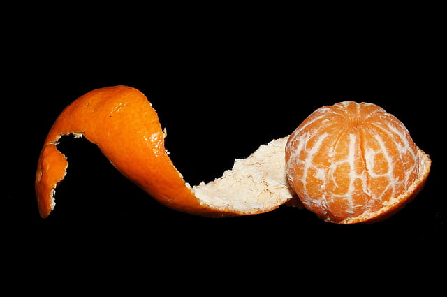 Against a black background, the twisted peel is stretched out to the left of a whole orange.