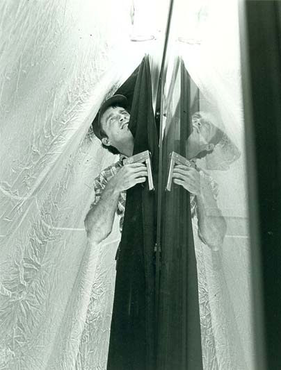 A black-and-white photo of a man adjusting lighting and surrounded by folds of fabric.