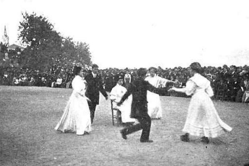 A vintage black-and-white photo of people doing a round dance in the park.