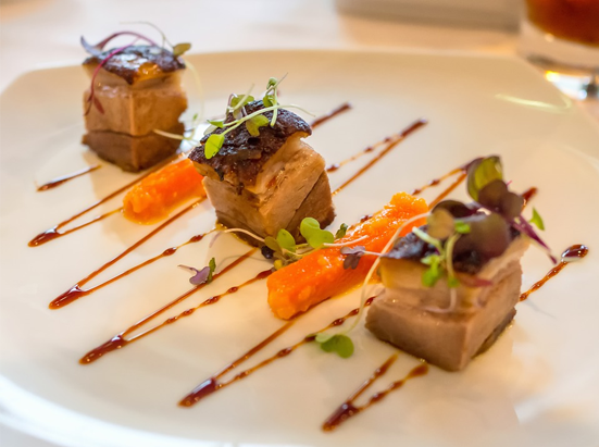 Three cubes of pork layers garnished with watercress, carrots between the cubes, and a zigzag of glaze on the white plate
