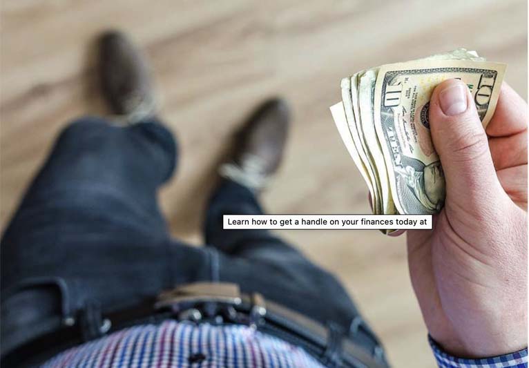 A look-down angle of a man's waist and legs with his right hand holding a wad of cash.