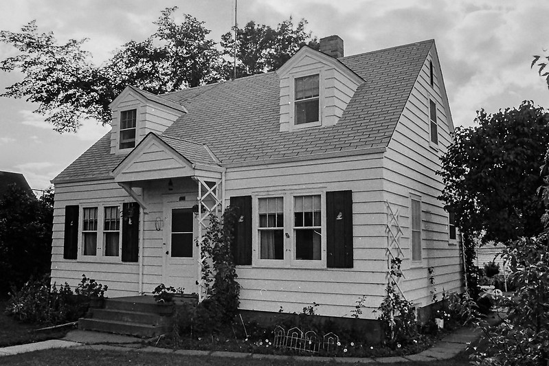 A black-and-white photo in an angled shot of a Cape Cod house with two dormers