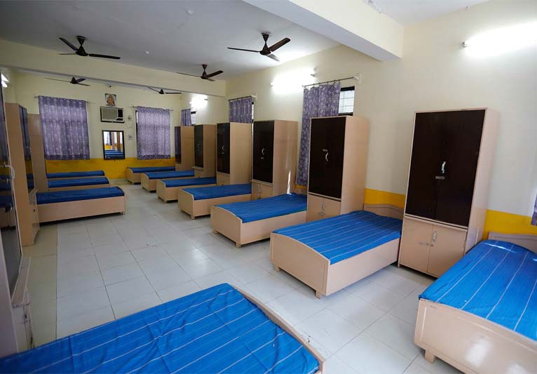 A pastel yellow room with ten single beds with royal blue bedspreads.