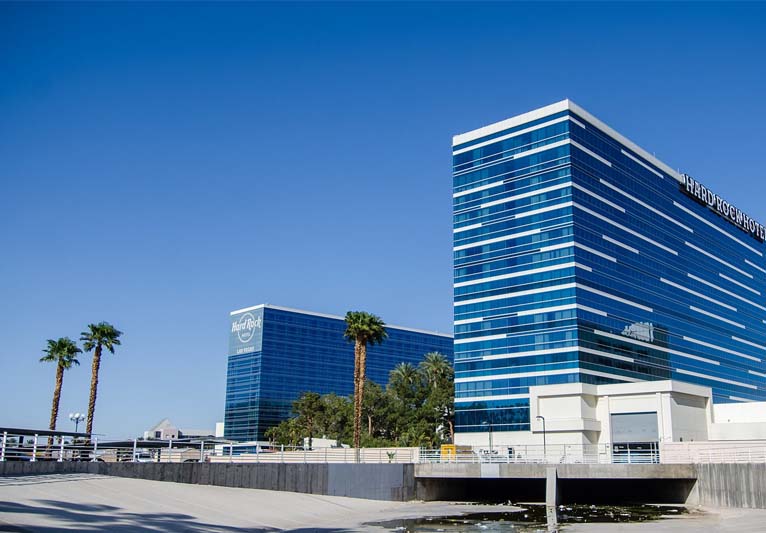 In the foreground is a huge parking lot with two tall blue buildings of glass with palm trees.