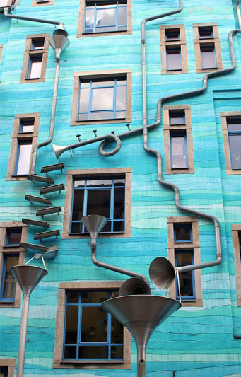 The bright blue side of a four-story house and a puzzle of downspouts swirling and twirling down the side.