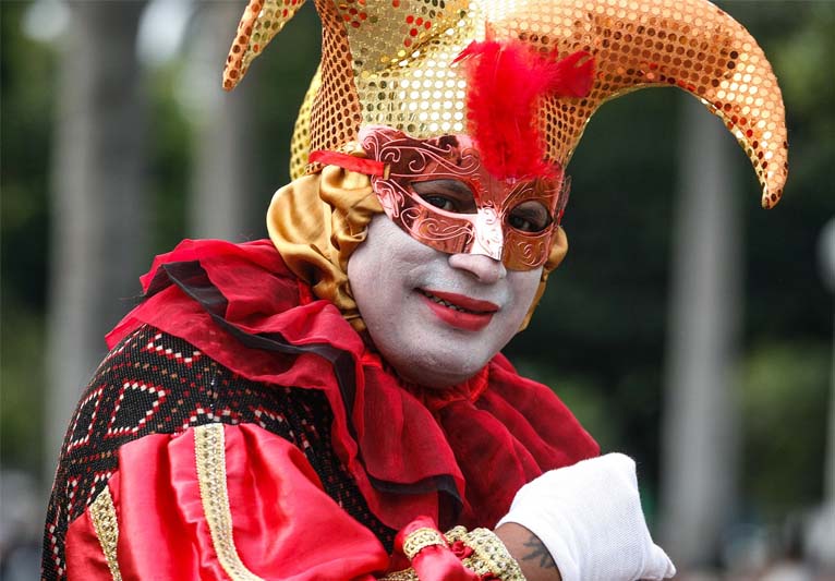 A bust shot of a white-faced jester in red with a gold two-pointed hat.