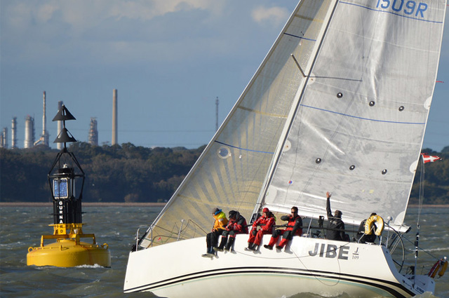 A sailboat heeling over as it goes around a yellow buoy.