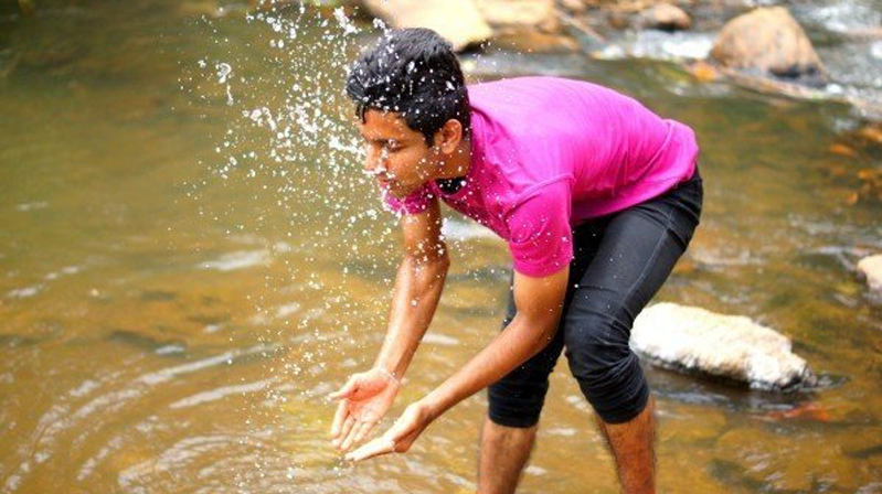 Young man in bold pink shirt and rolled up trousers, splashing water onto himself.