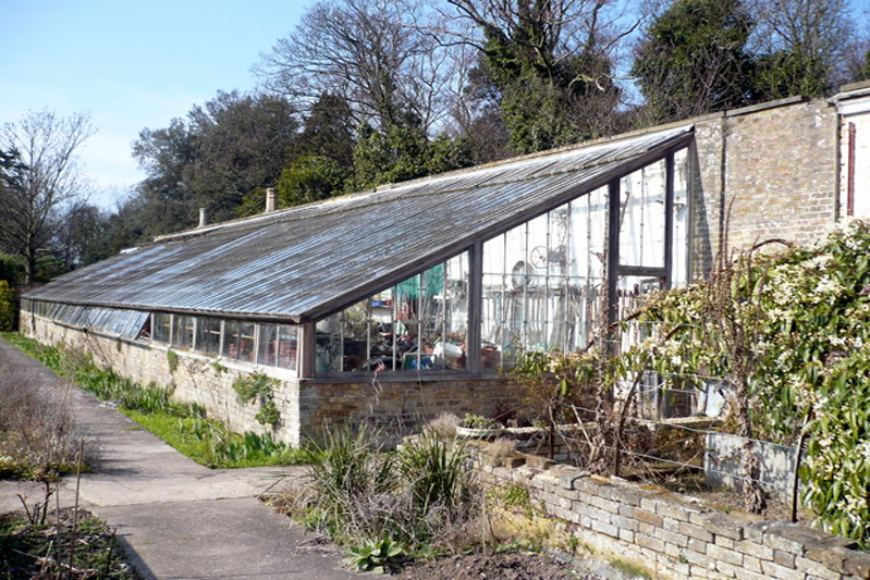 The roof of a glass greenhouse leans against an old wall